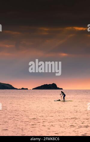 Eine weibliche Stand Up Paddlebarderin paddelt während eines goldenen Sonnenuntergangs in der Fistral Bay in Newquay in Cornwall. Stockfoto