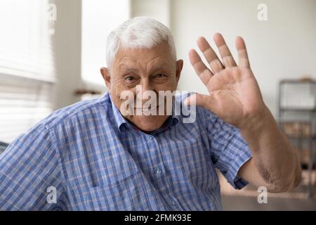 Glücklich lächelnder älterer Mann, der die Kamera anschaut, die Hand hallo winkt Stockfoto