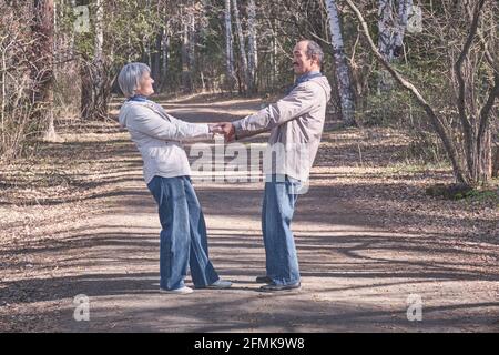 Ältere interrassische Paare in legerer Kleidung in einem Waldpark im Frühling, einander gegenüberstellend, lächelnd, Hände haltend, in voller Länge Stockfoto