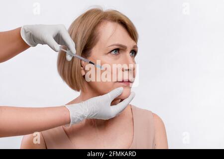 Charmante ältere Frau bekommen Gesichtslift Schuss über hellen Studio-Hintergrund. Nicht erkennbare Kosmetikerin oder plastischer Chirurg, die Schönheitsspritze macht, um zu attr Stockfoto