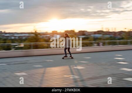 Junges Mädchen auf einem Skateboard in der Stadt. Aufnahme mit einem fotografischen Schwenken, mit verschwommenem Hintergrund. Konzept des nachhaltigen Transpors Stockfoto