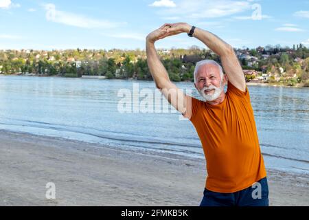 Ein glücklicher, energischer Rentner, der sich am Strand ausdehnt und am Fluss eine Seitenbeugeübung macht. Speicherplatz kopieren. Stockfoto