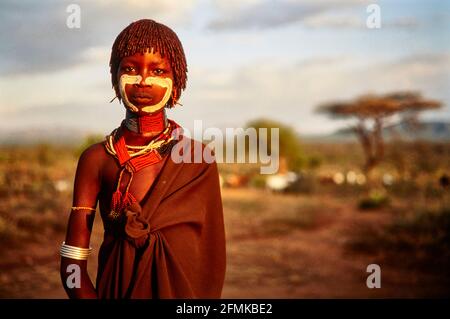 Ein junges Hamar-Mädchen, mit bunten Halsketten, Armbändern und einer Schürze aus Ziegenleder aus dem Dorf Gabo im Licht der untergehenden Sonne. 16.02.2007 Stockfoto