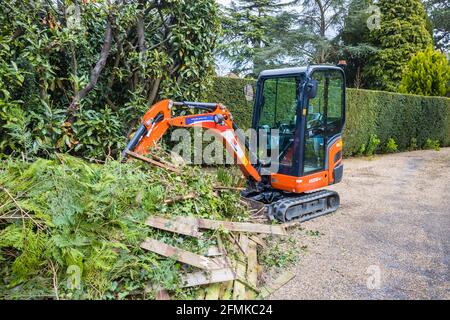 Ein Gummi-Raupenfahrzeug, ein orangefarbener Minibagger Kubota KX016-4, der für die Gartenräumung und die Beseitigung von Schutt verwendet wird, Surrey, England Stockfoto