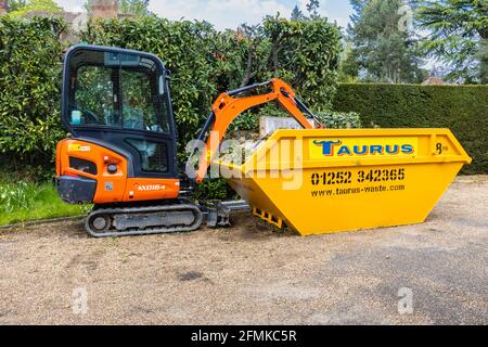 Ein Gummifahrzeug mit Raupen, ein orangefarbener Minibagger Kubota KX016-4 und ein gelber überlauf, der für die Gartenreinigung und die Beseitigung von Schutt verwendet wird, Surrey, England Stockfoto