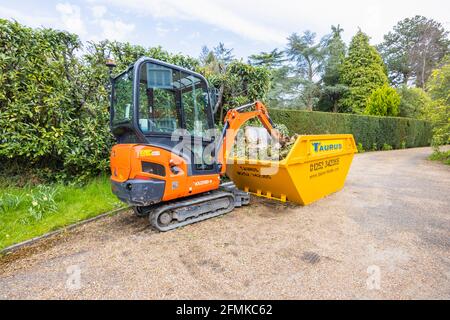 Ein Gummifahrzeug mit Raupen, ein orangefarbener Minibagger Kubota KX016-4 und ein gelber überlauf, der für die Gartenreinigung und die Beseitigung von Schutt verwendet wird, Surrey, England Stockfoto