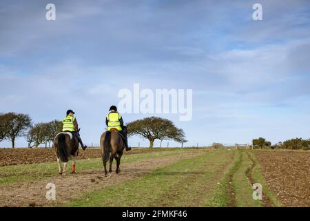 Zwei Frauen reiten auf Pferden in gut sichtbaren Jacken auf den South Downs in der Nähe von Ditchling, Sussex, England Stockfoto