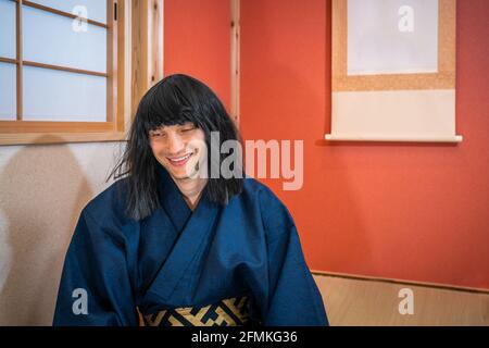 Traditionelle Papierschiebetüren in Japan mit Mann in kimono Kostüm und schwarze Haare sitzen an Nische hängen Papier Blättern Sie fröhlich lächelnd Stockfoto