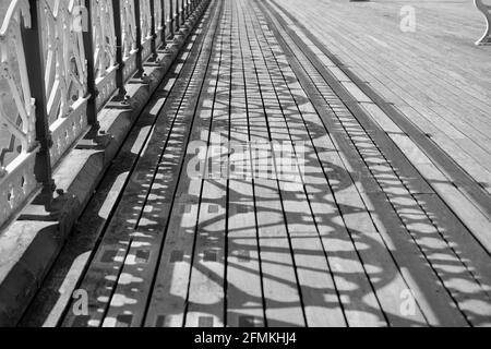 Monochrome Foto alten viktorianischen Pier und Promenade. Das Sonnenlicht strömt durch die komplizierten Designs, um Schattenmuster auf den Holzbrettern zu erzeugen Stockfoto