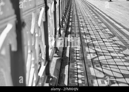 Monochrome Foto alten viktorianischen Pier und Promenade. Das Sonnenlicht strömt durch die komplizierten Designs, um Schattenmuster auf den Holzbrettern zu erzeugen Stockfoto