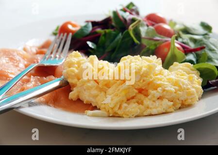 Köstlicher Teller mit Rührei, geräuchertem Lachs und Salat mit Messer und Gabel Stockfoto