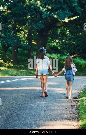 Seltene Ansicht von zwei jungen Mädchen, die Hand in Hand im Park im Freien gehen, London, Großbritannien Stockfoto