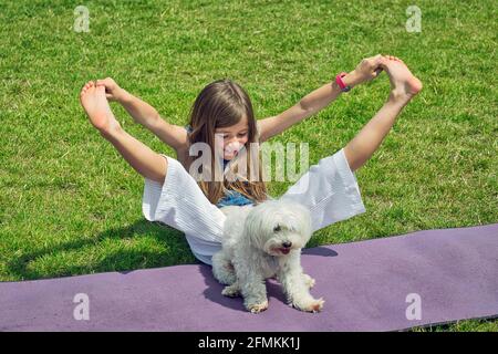 Mädchen mit Hund tut Yoga-Übungen in der Natur im Freien auf Grünes Gras auf der Fitnessmatte, Primerose Hill Park, London, Großbritannien Stockfoto