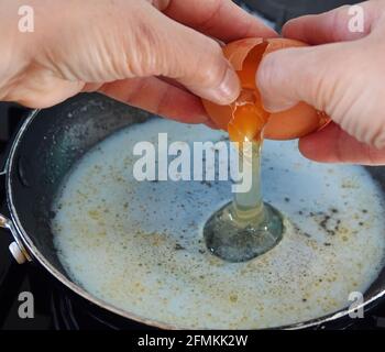Nahaufnahme eines Eies, das geknackt und in ein gegossen wurde Pfanne auf dem Ofen - Rühreier machen Stockfoto