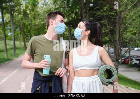 Junge Sport-Paare, die einander anguchten und lachen, tragen schützende Gesichtsmasken. Fitness während einer Coronavirus-Pandemie. Stockfoto