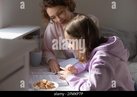 Fürsorgliche junge Mutter hilft Teenager-Kind mit Hausaufgaben.