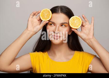 Glückliche ziemlich gesunde Frau mit klarer Haut und geradem Haar mit Zitronenfrüchten auf weißem Hintergrund. Konzept für Ernährung, Hautpflege und Gesichtsbehandlung Stockfoto