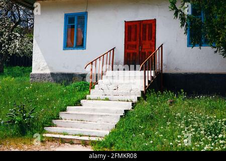 Haus mit roter Tür und weißer Treppe. Haus im Dorf mit weißen Wänden. Altes rustikales Haus Stockfoto