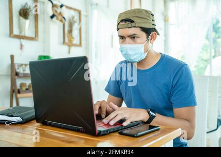 Freiberuflicher asiatischer Mann im Hemd trägt Gesichtsmaske arbeiten mit Laptop im Coffee Shop, um die Ausbreitung der zu verhindern Coronavirus oder COVID-19 Stockfoto