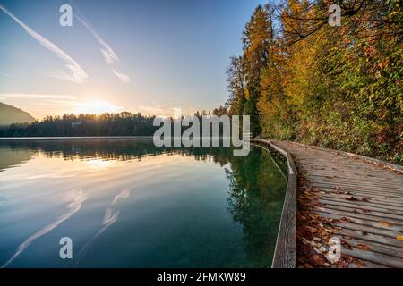 Touristenroute auf dem Holzboden entlang des berühmten alpinen Bleder Sees (Blejsko jezero) in Slowenien, erstaunliche Herbstlandschaft. Landschaftlich schöner Blick auf den See Stockfoto