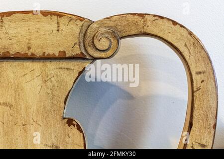 Ein Teil eines alten, geschwungenen Holzstuhls wirft Schatten auf die weiße Wand dahinter. Stockfoto