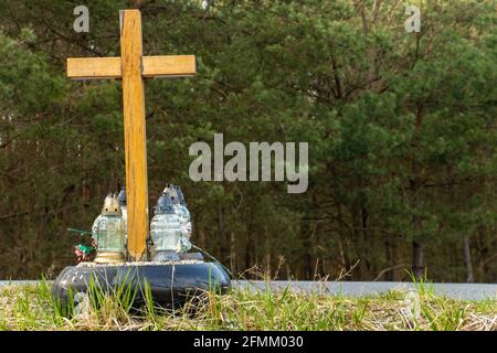 Ein Gedenkkreuz am Straßenrand mit Kerzen zum Gedenken an den tragischen Tod an einer Straße. Stockfoto