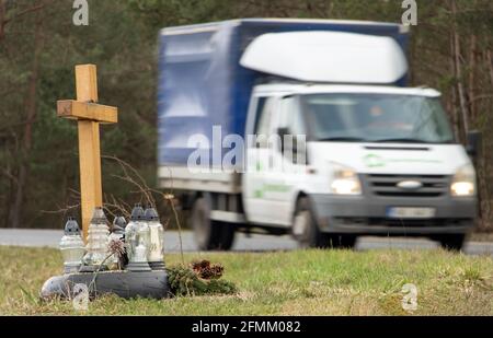 Ein Gedenkkreuz am Straßenrand mit Kerzen zum Gedenken an den tragischen Tod, auf einer Fahrt im Hintergrund verschwommener Lastwagen Stockfoto