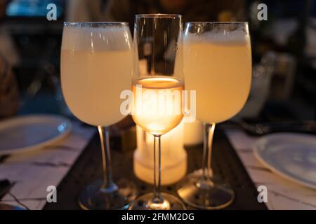 Glas Roséwein zwischen Pisco sauer großen Gläsern mit Kerzenlicht dahinter. Ausgefallenes Restaurant, Abendessen, Getränke, Feier Konzepte Stockfoto