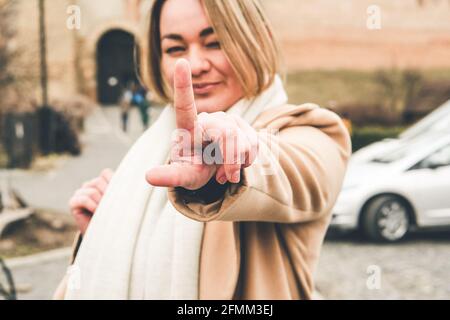 Fröhliche lächelnde Frau. Eine einzige Frau flirtet und zwinkert ein Auge, zeigt den Finger nach oben, selektive Fokussierung auf den Finger, verschwommene Fotografie, Filmgeräusche Stockfoto