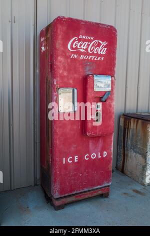 Ein leuchtend roter Coca-Cola-Verkaufsautomat, der mit Original intakt ist Teile und einige Patina stehen senkrecht im Freien gegen ein Gebäude Stockfoto