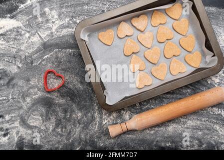 Holz-Nudelholz und Backblech mit herzförmigen Plätzchen. Hausgemachtes Backen. Stockfoto