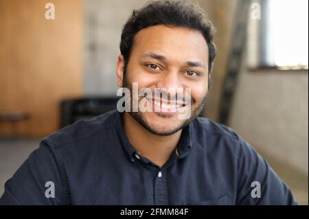 Fröhlicher und heiterer hindu-Mann in elegantem Casual-Hemd, Kopfschuss eines jungen, hübschen indianers, hübscher Mann mit gemischter Rasse blickt mit toothy Lächeln auf die Kamera Stockfoto