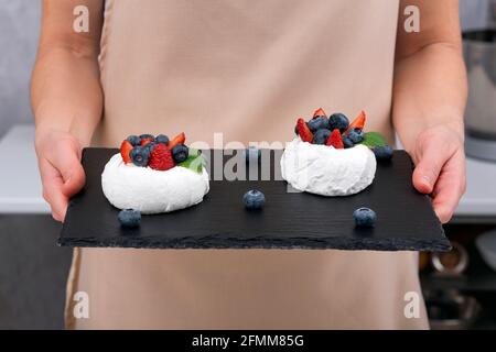 Anna Pavlova auf schwarzem Tablett in den Händen der Frau backen. Baiser-Kuchen mit frischen Beeren. Stockfoto