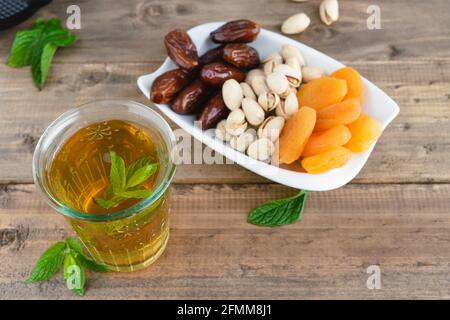 Obstschale mit Datteln, Pistazien und getrockneten Aprikosen mit Teeglas auf Holzboden. Speicherplatz kopieren. Stockfoto