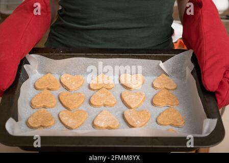 Herzen aus Teig auf einem Backblech in den Händen eines Bäckers geschnitten. Nahaufnahme. Stockfoto