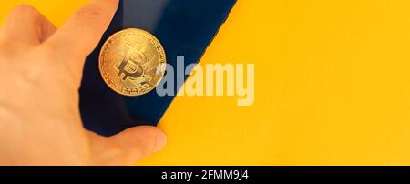 Konzept des Menschen mit Smartphone mit Bitcoin-Münze zum Einkaufen, Bannerfoto mit gelbem Hintergrund Stockfoto