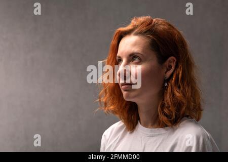 Porträt einer rothaarigen Frau auf grauem Hintergrund Seitenansicht Stockfoto