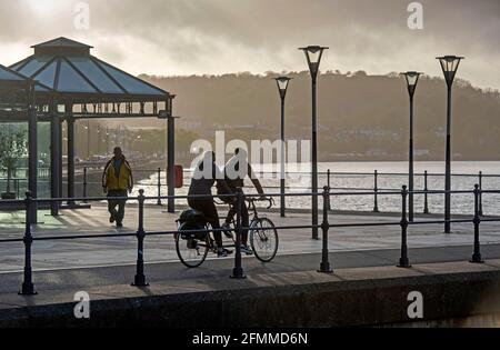 Swansea, Großbritannien. Mai 2021. Ein Paar fährt heute Abend mit dem Tandemrad an Verdis Eisdiele am Strandweg im kleinen Küstendorf Mumbles in der Nähe von Swansea vorbei und macht eine Pause bei nassem und windigem Wetter. Quelle: Phil Rees/Alamy Live News Stockfoto