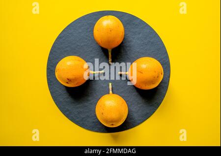 Passiflora ligularis. Süße Granadilla. Drei süße Passionsfrucht auf schwarzem und gelbem Hintergrund. Farbbild. Stockfoto