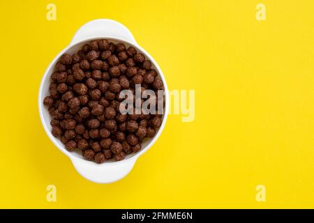 Schokolade Müslischale isoliert auf gelbem Hintergrund, Schokoladenkugeln, gesundes Frühstück Stockfoto