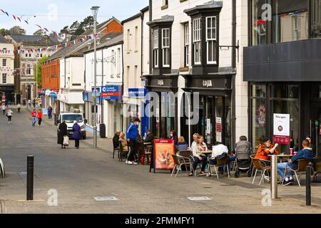 Bridgend, Wales - April 2021: Menschen, die vor einem Café in der Caroline Street, einer Fußgängerzone im Einkaufszentrum der Stadt, an Tischen sitzen Stockfoto