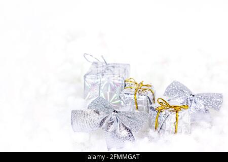Helle silberne Weihnachtsdekorationen (Bänder, Geschenke, Geschenkboxen) auf weißem Kunstschneegrund mit Kopierfläche. Weihnachten und Neujahr traditionell Stockfoto