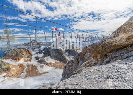 Frau auf Hängebrücke mit Schweizer Flagge. Titlis Klippenwanderung mit Gletscher in den Uri Alpen. Aussichtspunkt auf 3028 Metern in der Sommersaison, Kanton Bern Stockfoto