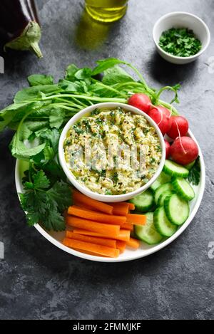 Baba ganoush (geröstete Auberginen-Dip) und frisches Bio-Gemüse auf dem Teller auf Steingrund. Gesunde Ernährung. Vegetarisches veganes Lebensmittelkonzept. Stockfoto