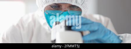Arzt in Schutzanzug und Brille schaut durch das Mikroskop Stockfoto