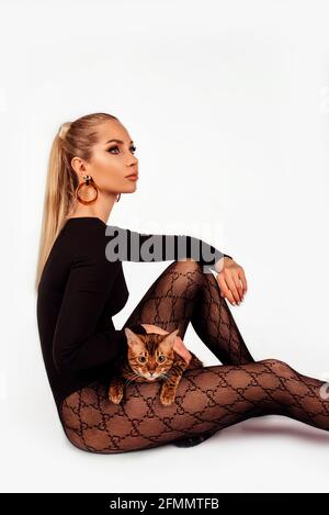 Porträt einer attraktiven jungen blonden Frau mit einer bengalischen Katze. Ein schönes Mädchen, das auf dem Boden sitzt, sieht zur Seite, elegante Frisur Stockfoto