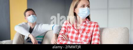 Beleidigte Frau und Mann sitzen auf der Couch und tragen Schutzkleidung Masken Stockfoto