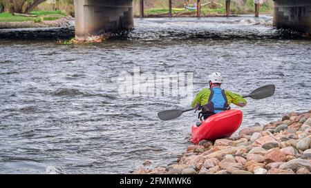 Kajakmännchen mit Trockenanzug, Helm und Schwimmweste starten ein Kajak im Poudre River Whitewater Park in Fort Collins, Colorado Stockfoto