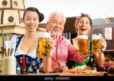 Im Pub - Freunde in Tracht, Dirndl und Lederhosen ein frisches Bier in Bayern, Deutschland Stockfoto