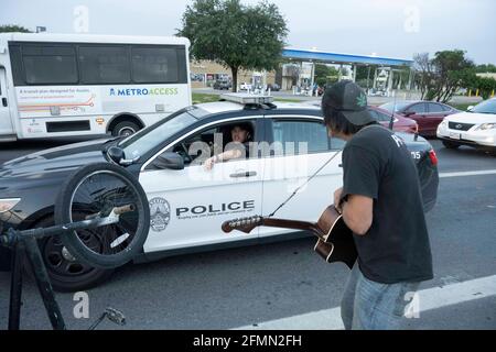 Austin, Texas, USA. Mai 2021. Der Musiker und Handwerker DOUGLAS CRAWFORD begrüßt einen Polizisten aus Austin, als er seine Gitarre für den Ersatzwechsel in der Nähe seines Lagers an der Ecke des Ben White Blvd. Und der South Congress Avenue in Austin, TX, anklimpelt, wo er seit über einem Jahr lebt. Crawford, 60, sagt, er bleibt für sich selbst und macht sich keine Sorgen über die neue obdachlose Niederschlagung von Austin und das Campingverbot ab Dienstag. Quelle: Bob Daemmrich/ZUMA Wire/Alamy Live News Stockfoto